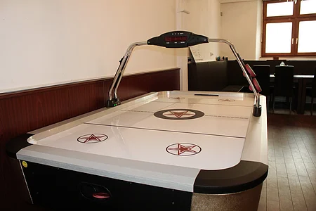 Airhockey-Tisch mit elektronischer Anzeige in einem Raum mit Holzboden und Fenster im Hintergrund.