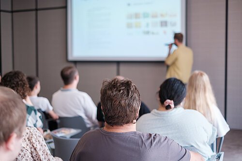Seminar/Vortrag Group of people attending educational seminar focused on speaker presenting digital content on screen