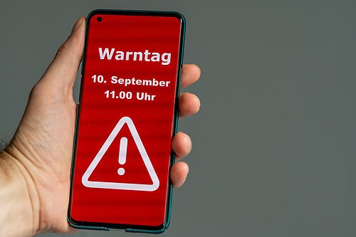 Symbolbild zum bundesweiten Warntag. Hand hält ein Mobiltelefon 10. September