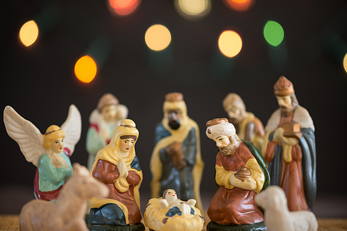 Krippenszene mit Figuren von Maria, Josef, Jesuskind, Hirten, Königen und Tieren vor unscharfem Hintergrund mit Lichtern.